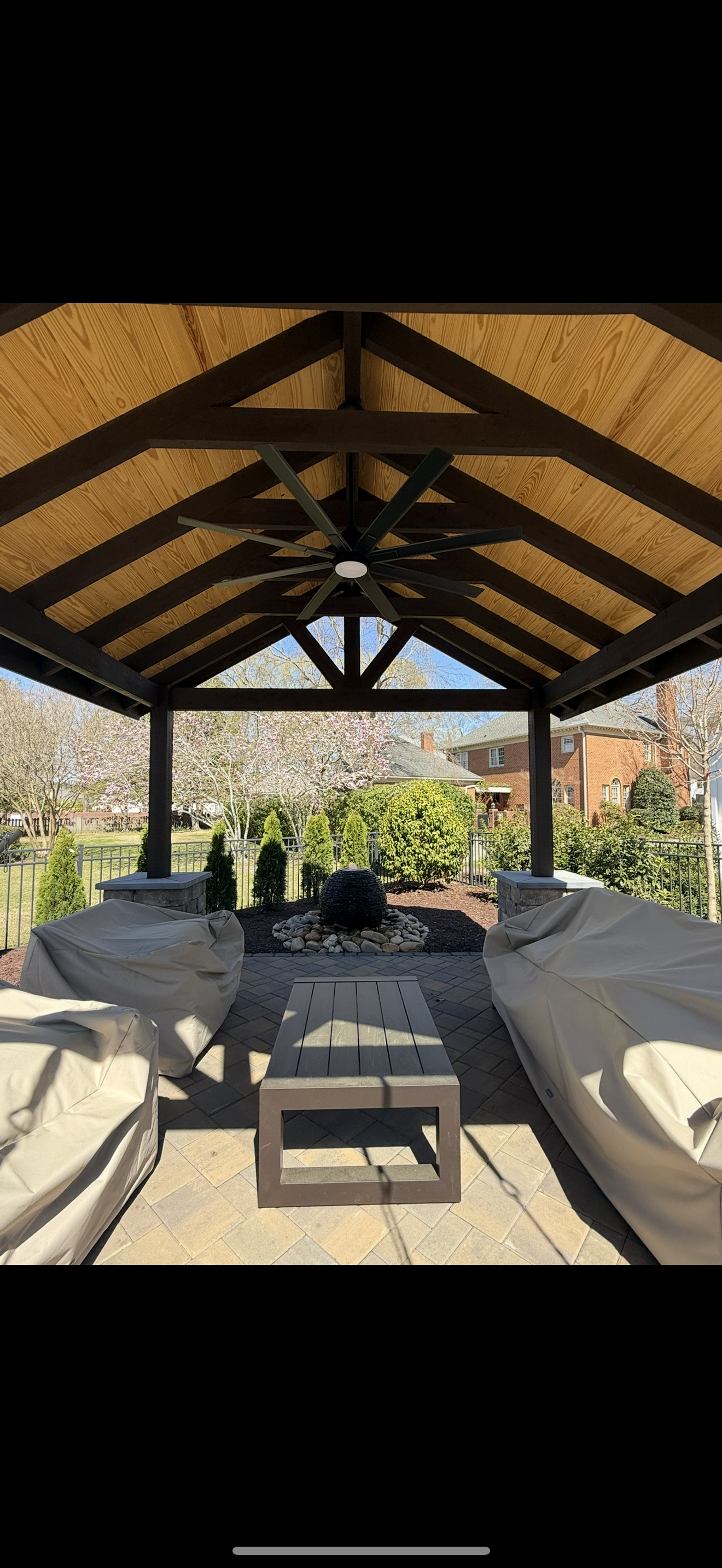 Gazebo with dark wooden beams and a light brown thatched roof. Furnished with covered seating and a coffee table.