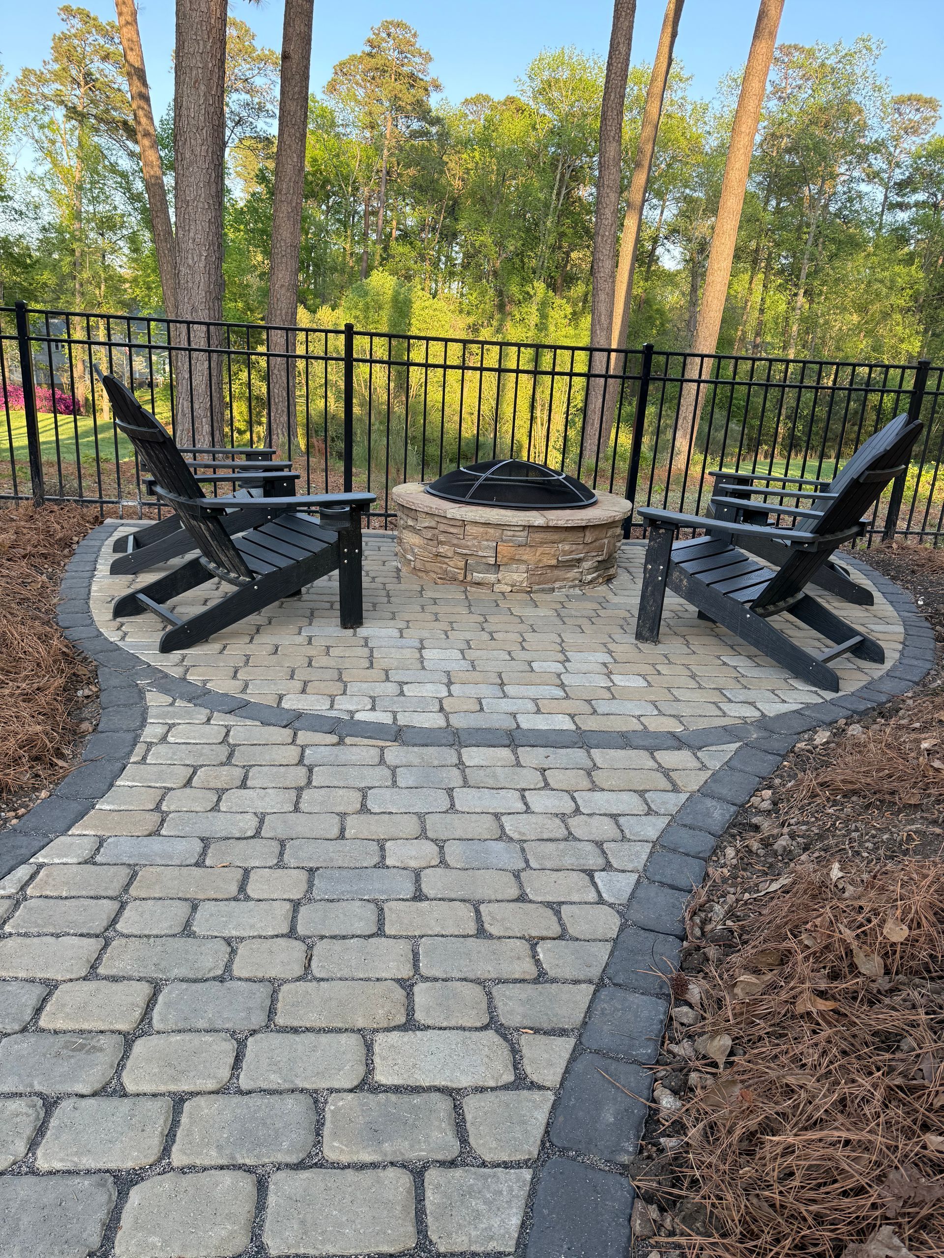 Brick patio with fire pit and Adirondack chairs, set within a fenced backyard.