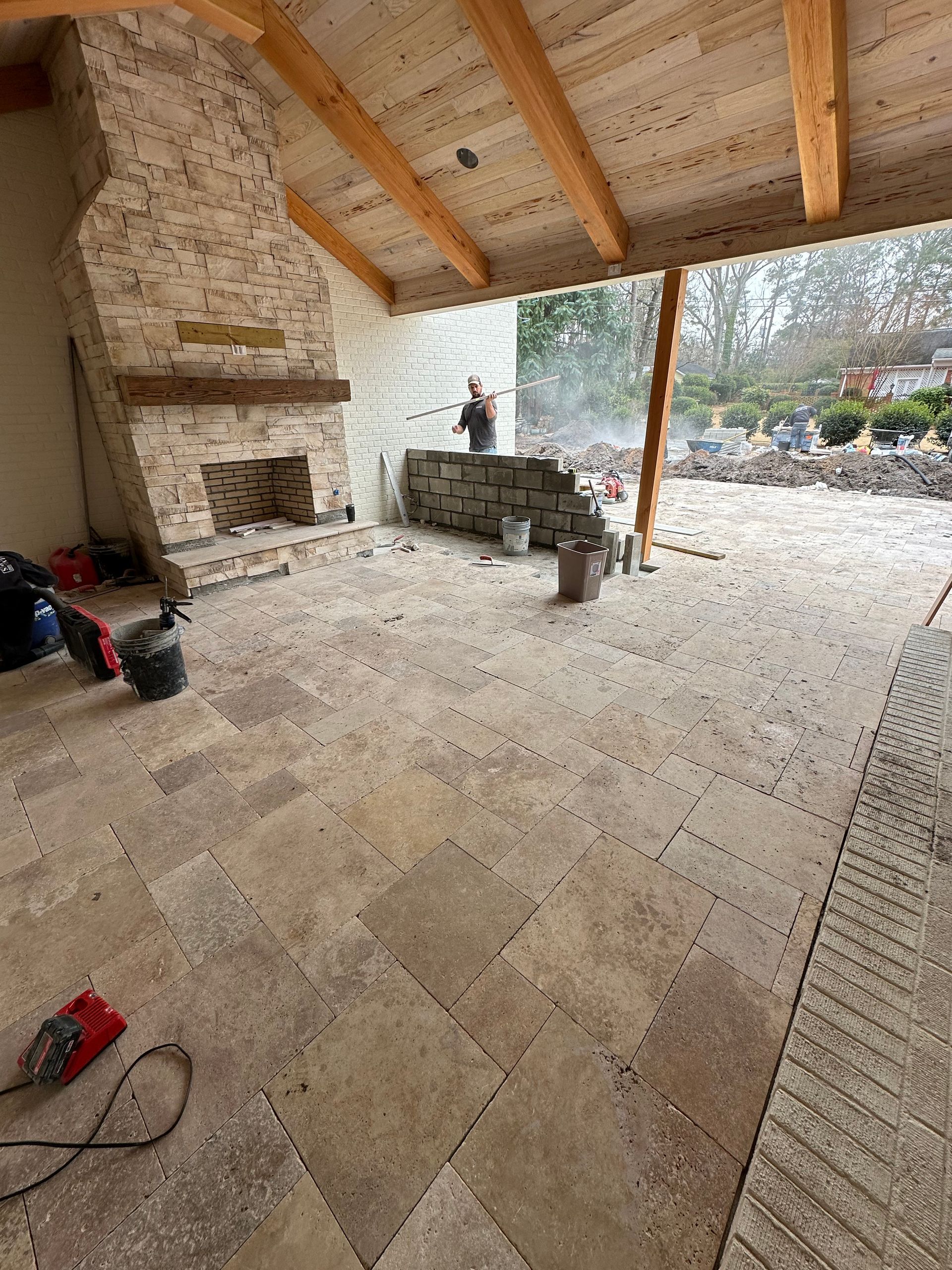Construction of a patio with stone flooring and fireplace. A worker is building a wall.