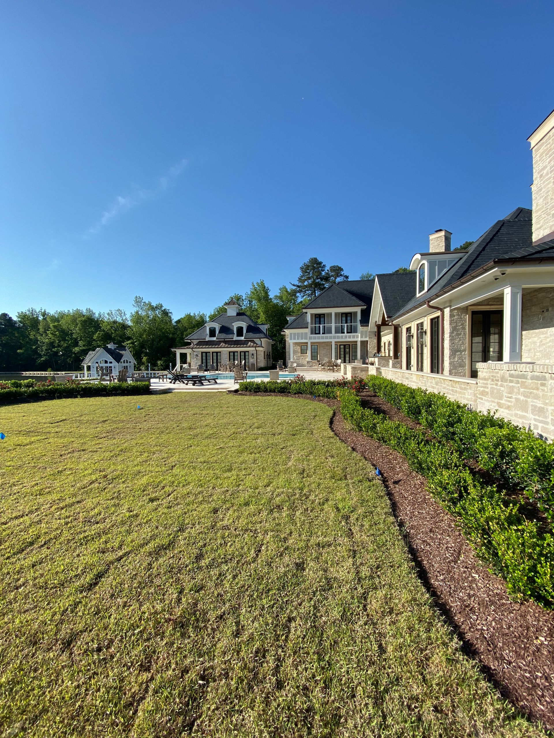 Sprawling estate with manicured lawn, landscaping, and a pool. Blue sky overhead.