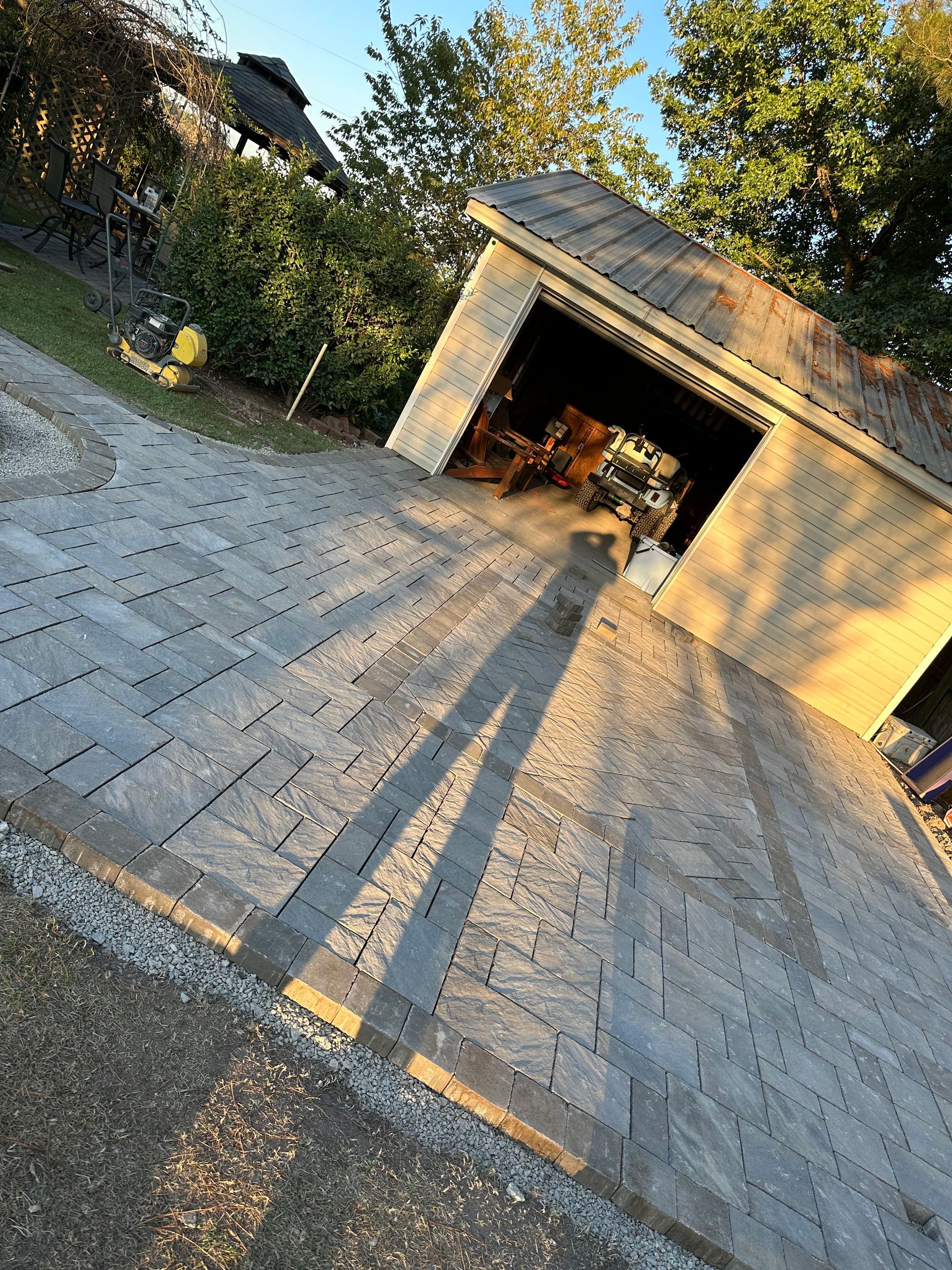 Brick driveway leading to a garage; sunlight casts long shadows.