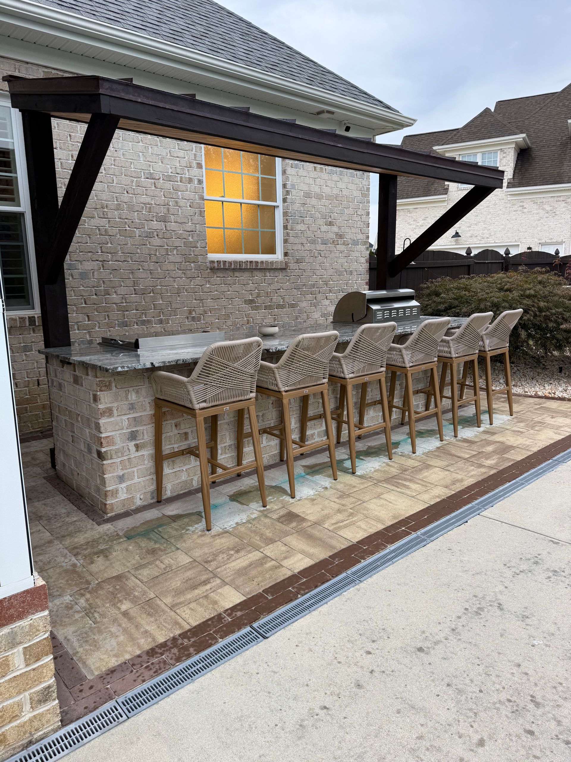 Outdoor kitchen with brick facade, bar seating, dark wood pergola, and grill.