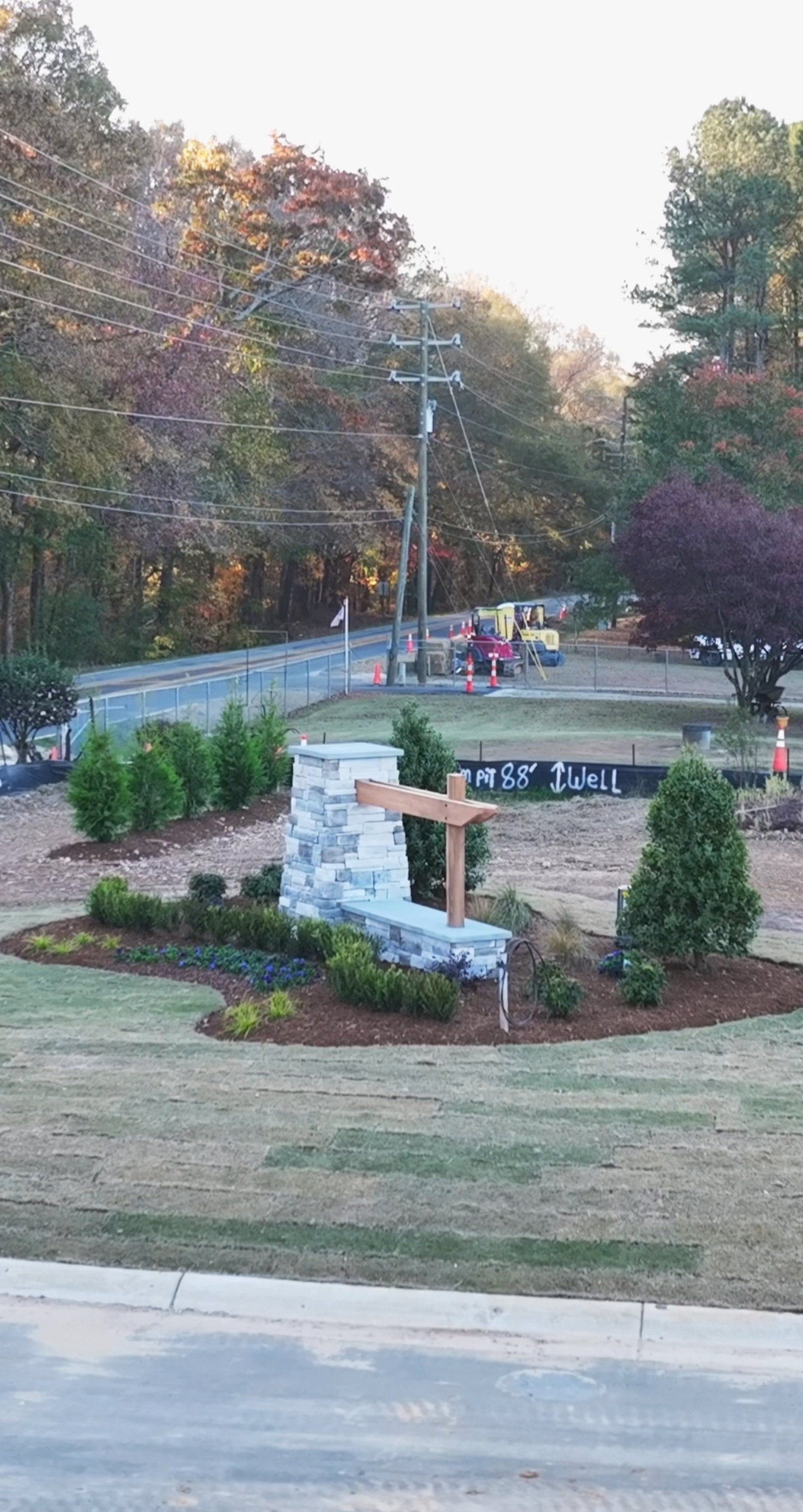 Stone monument with wooden beam, surrounded by landscaping, in front of a park with playground equipment.