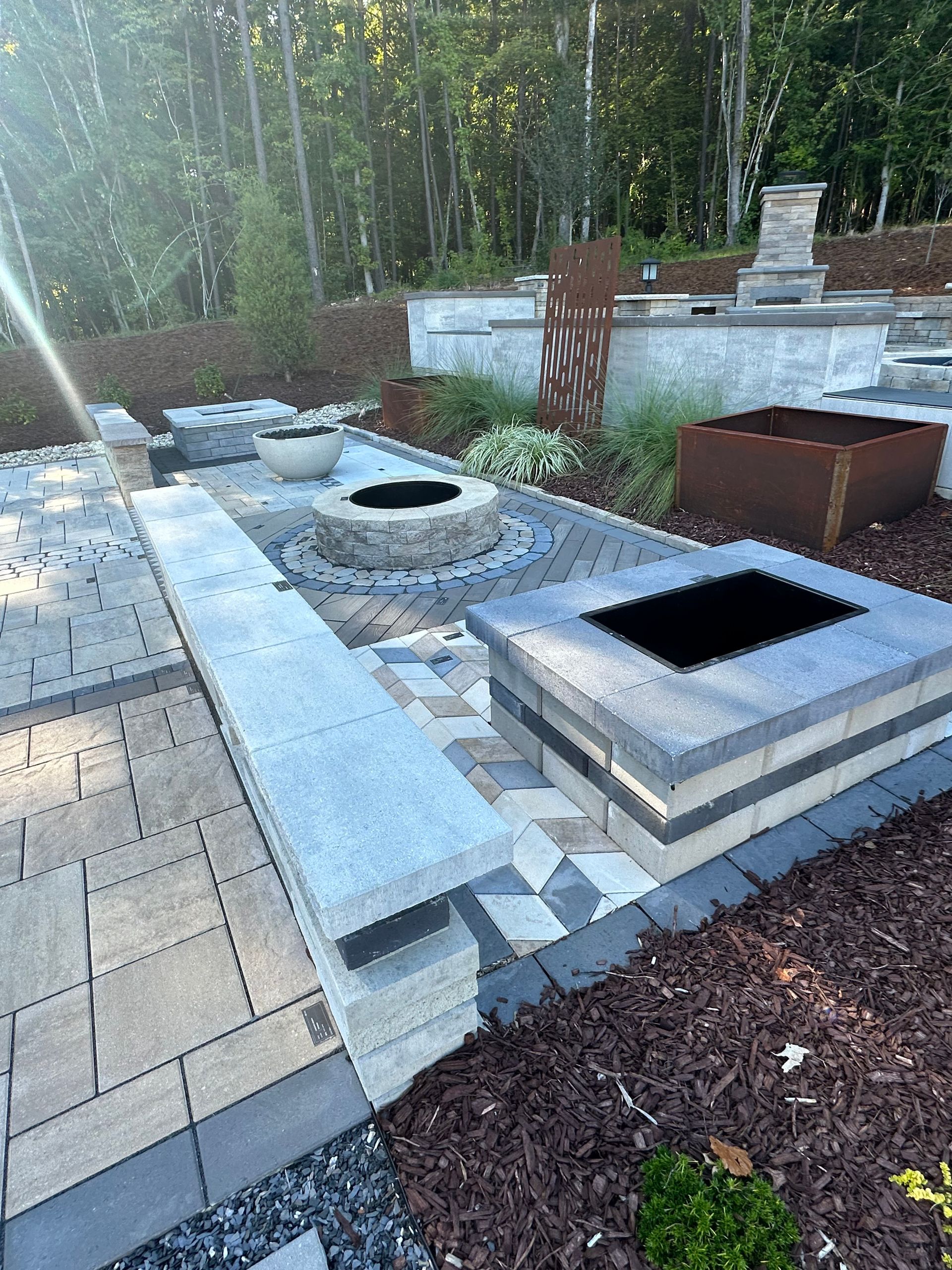 Outdoor patio with stone pavers, fire pits, and landscaping.