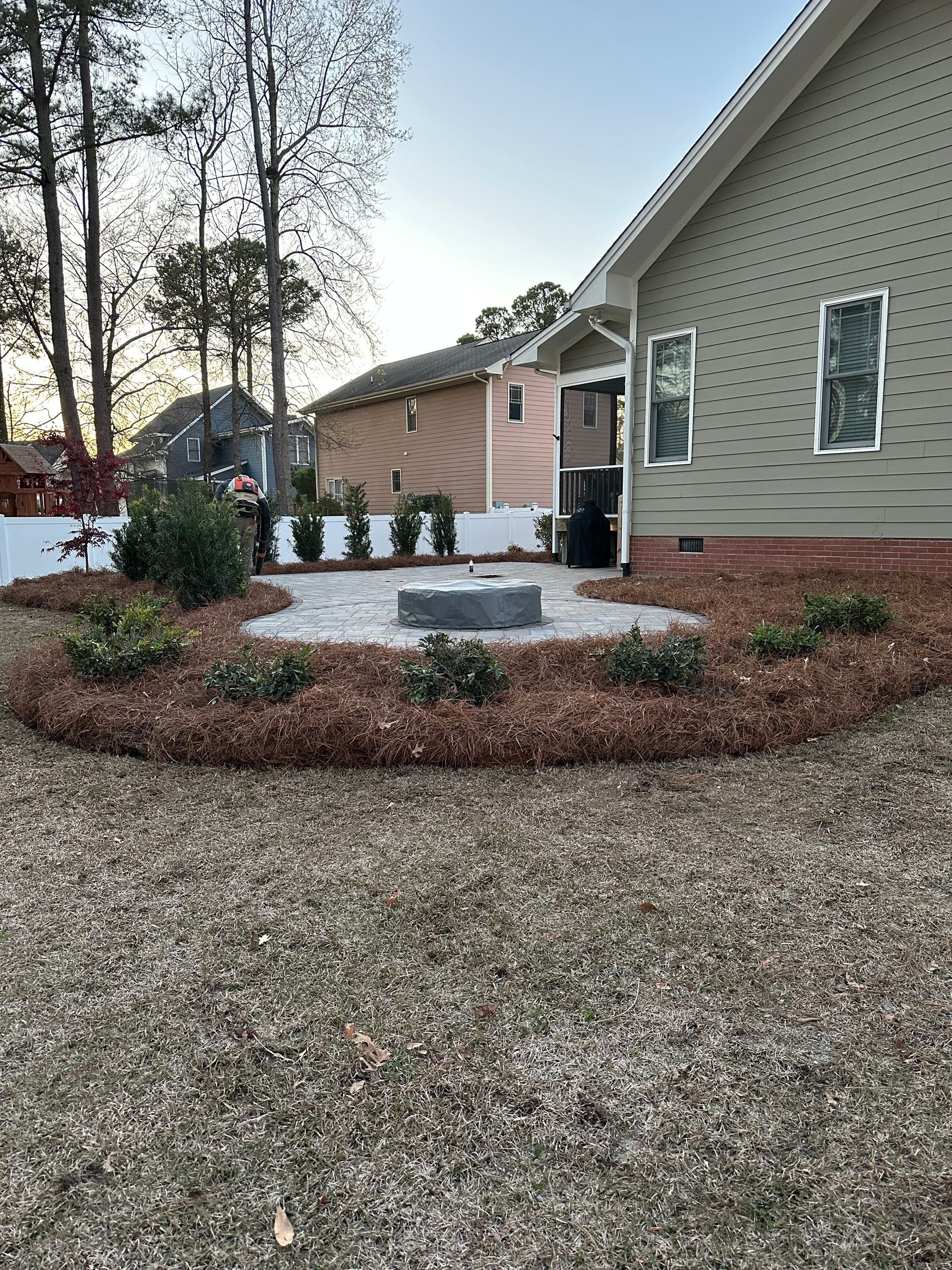 Backyard patio with fire pit, surrounded by mulch and landscaping, near a house.