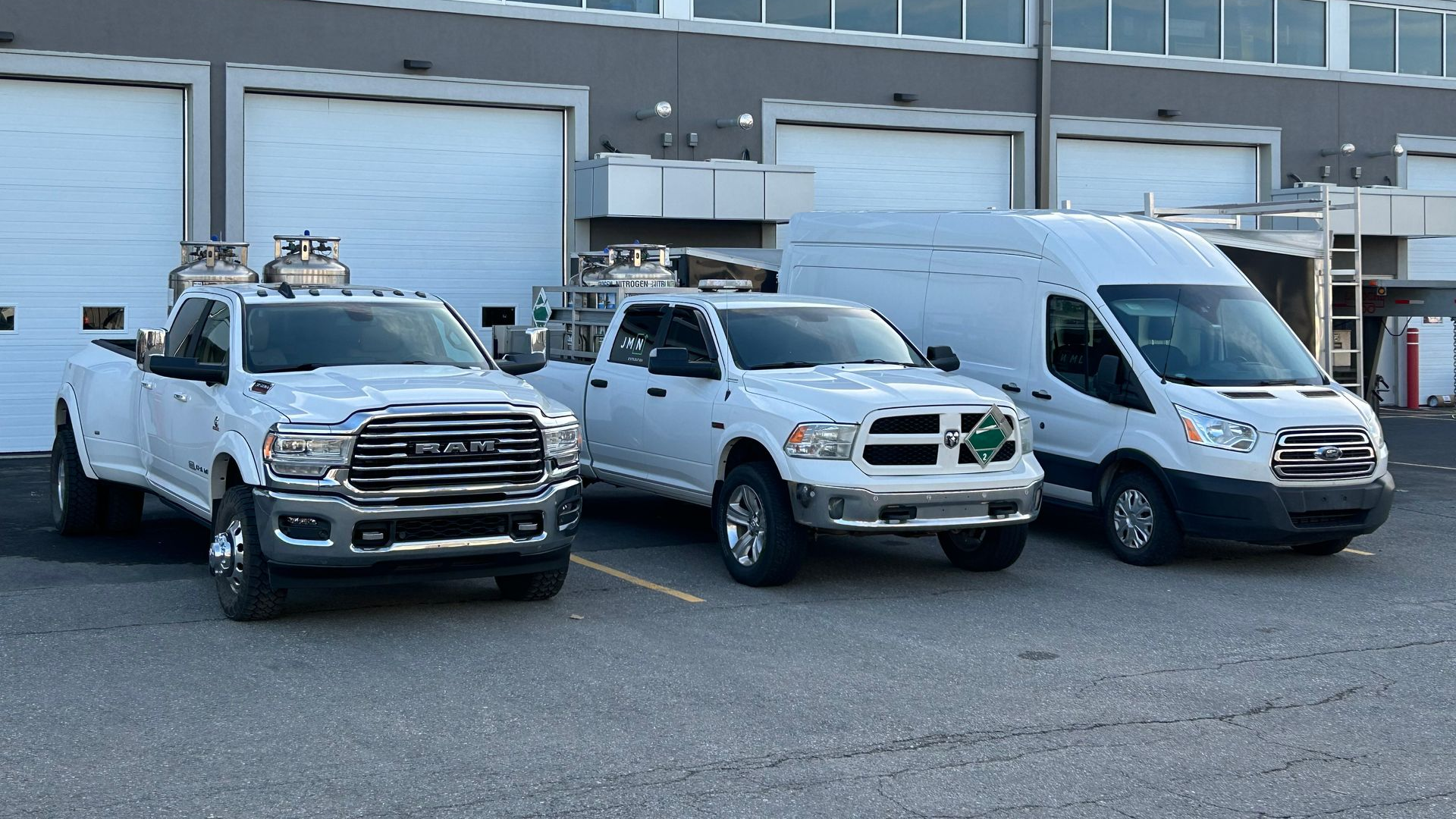Three white vehicles: a pickup truck, another pickup, and a van, parked in front of garage doors.