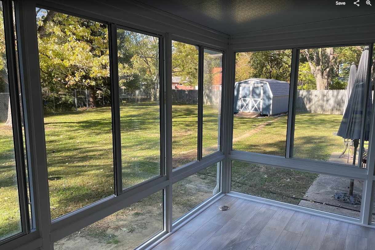 A view from inside a sunroom with large windows looking out onto a grassy backyard with a storage shed.