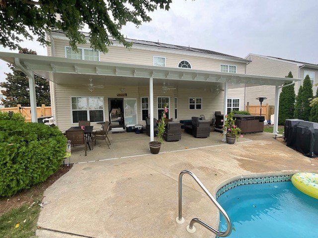 A backyard patio with a white covered porch, outdoor furniture, and a swimming pool in the foreground.