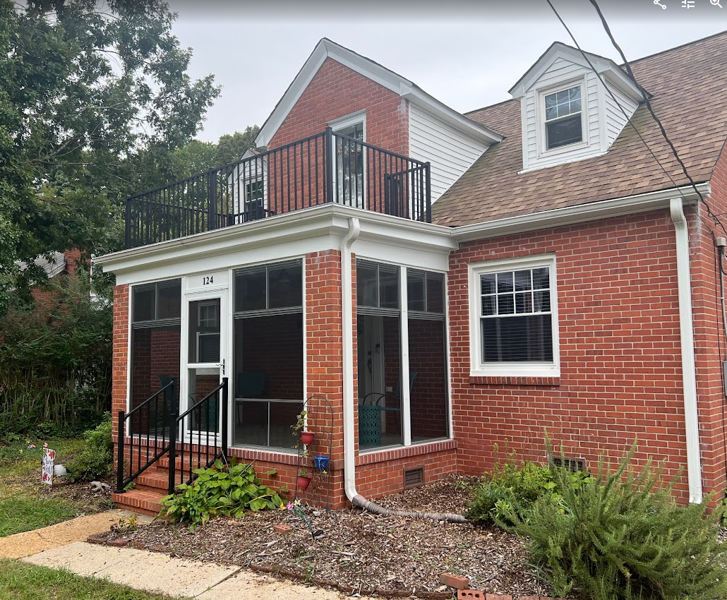 A red brick two-story house with a screened-in porch, a second-story balcony, and white decorative roof trim.
