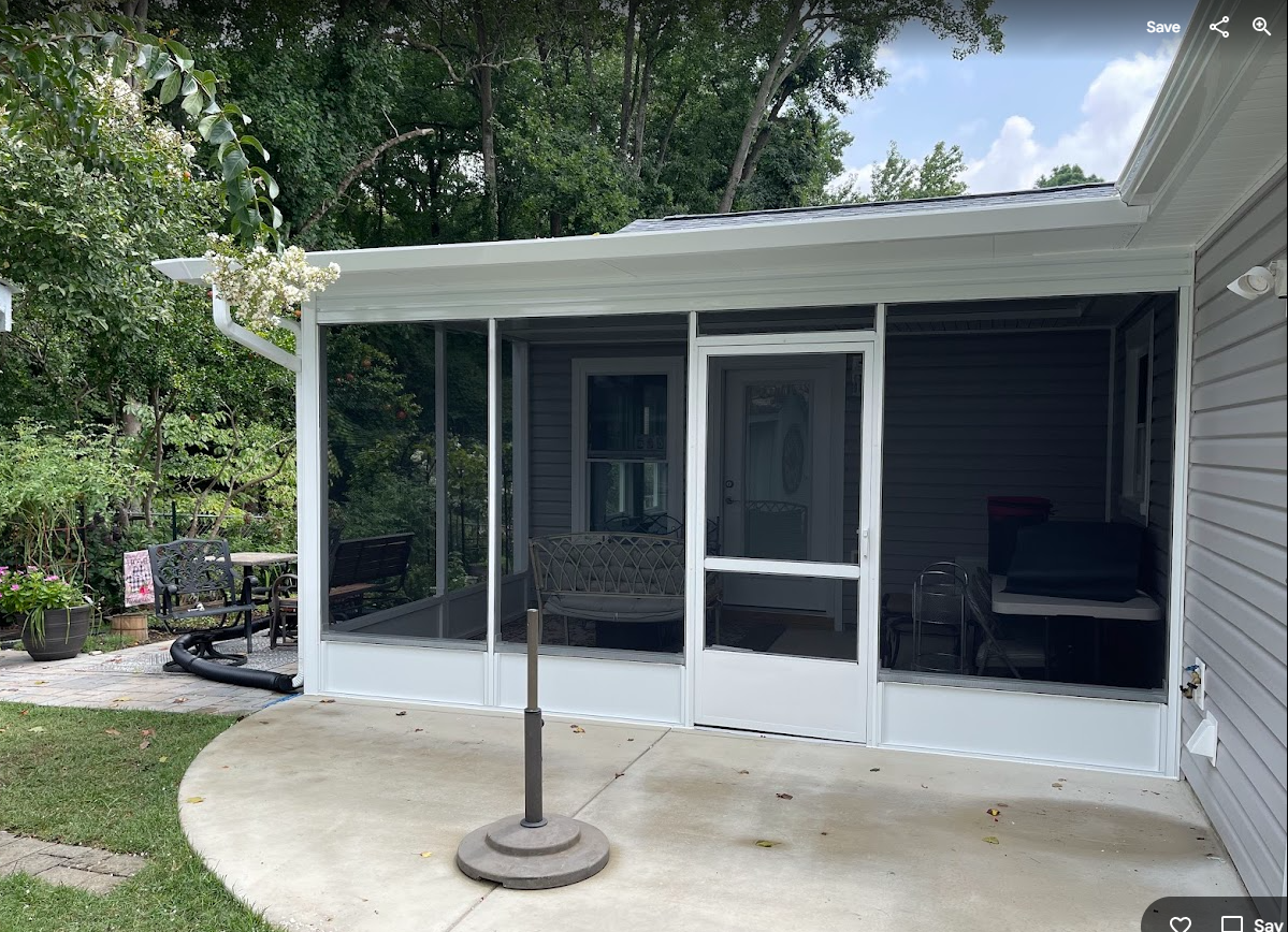 A white-framed screened-in porch with a screen door, attached to a gray house next to a concrete patio.