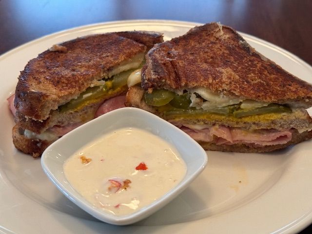 Cuban sandwich cut in half on a white plate, served with a small dish of dipping sauce.