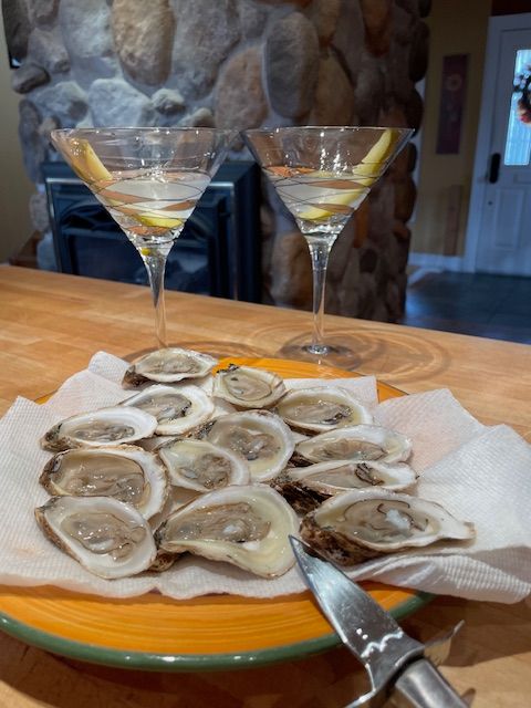 Plate of raw oysters on a paper towel, with two martini glasses. A shucking knife is beside the plate.