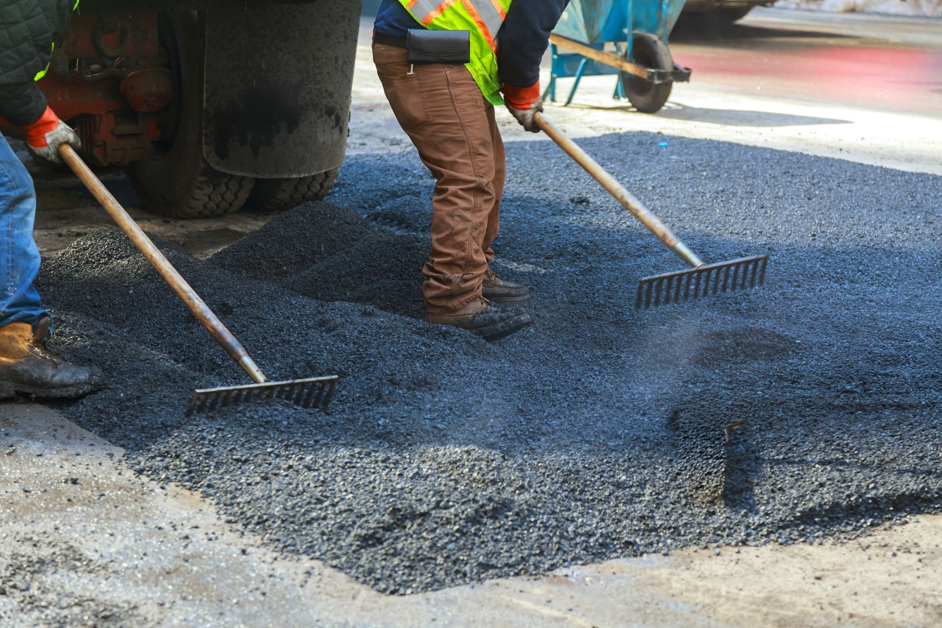 Workers raking fresh blacktop as part of professional commercial asphalt services on a parking lot.
