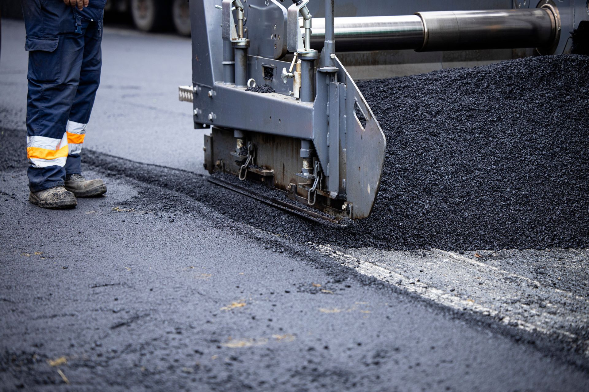 Road paving machine laying fresh asphalt beside a worker’s boots