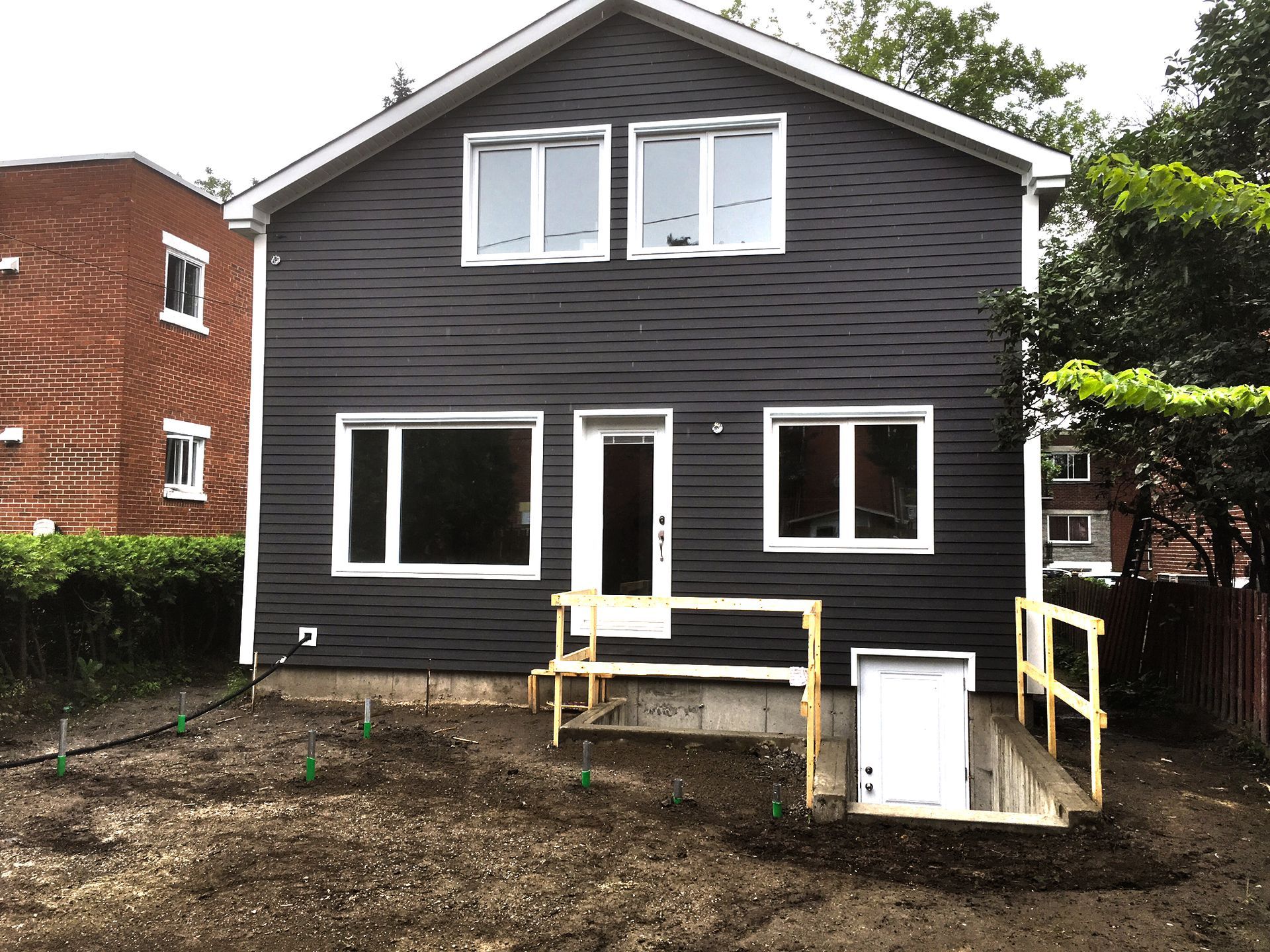 Two-story house with dark gray siding, white trim windows, and a basement entrance with a ramp.