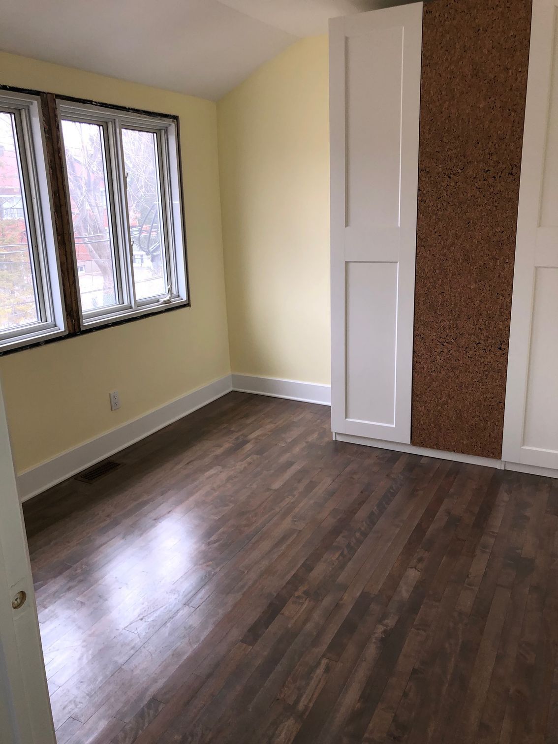 Empty bedroom with dark wood floor, yellow walls, white trim, and a window.