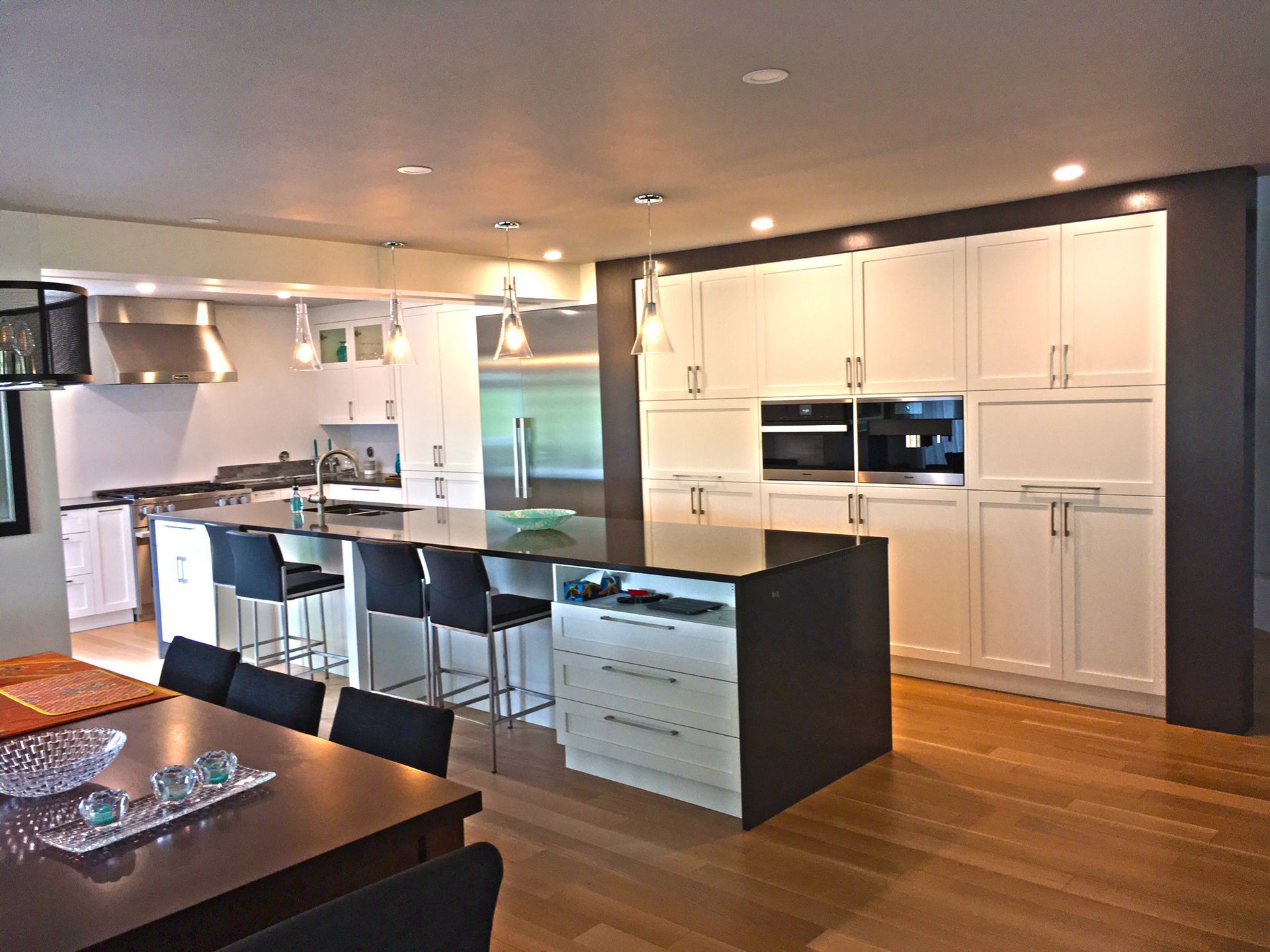Cuisine moderne avec armoires blanches, îlot foncé, appareils électroménagers en acier inoxydable et plancher en bois.