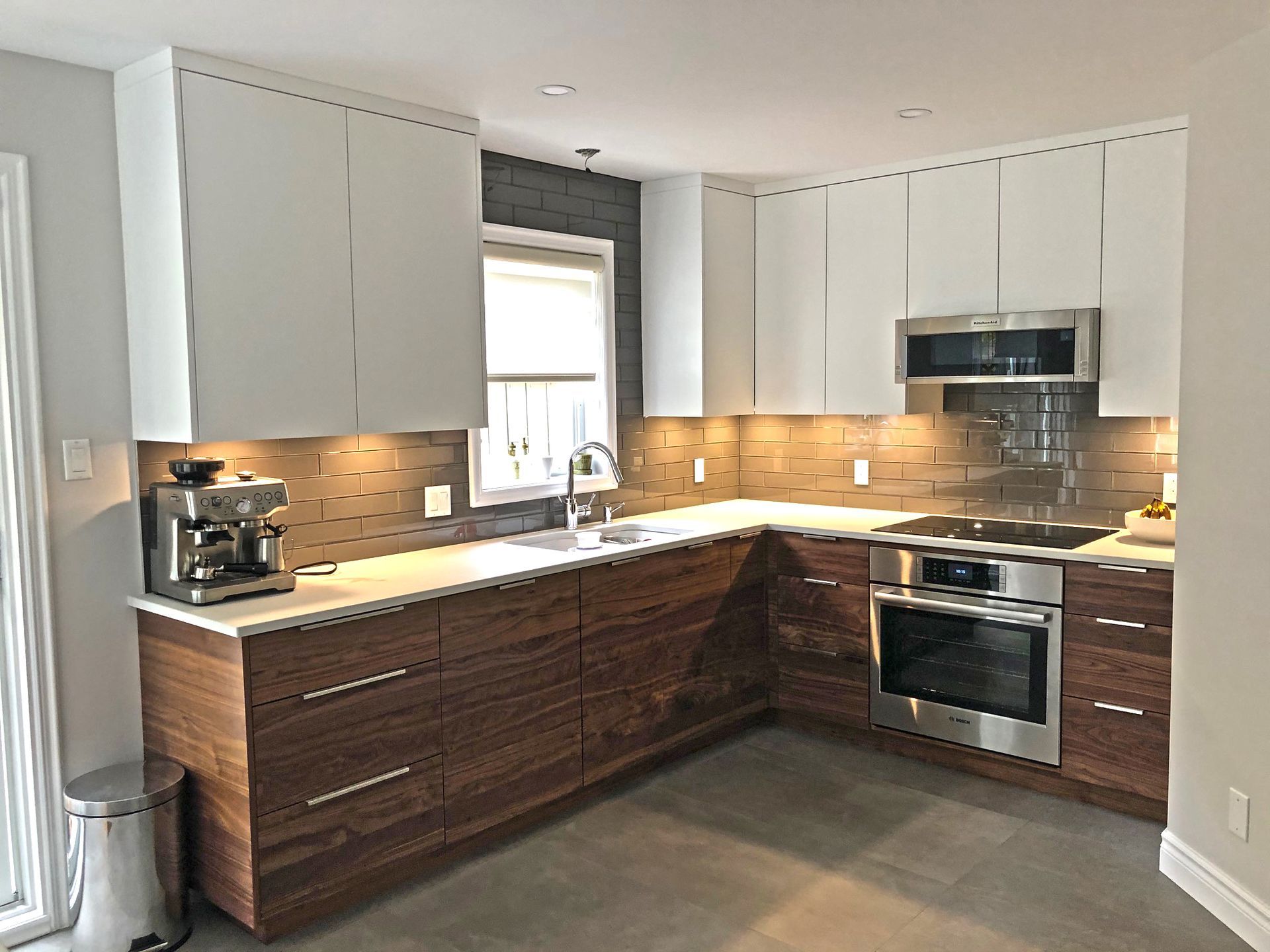 Modern kitchen with white upper cabinets, dark wood lower cabinets, stainless steel appliances, and a gray backsplash.