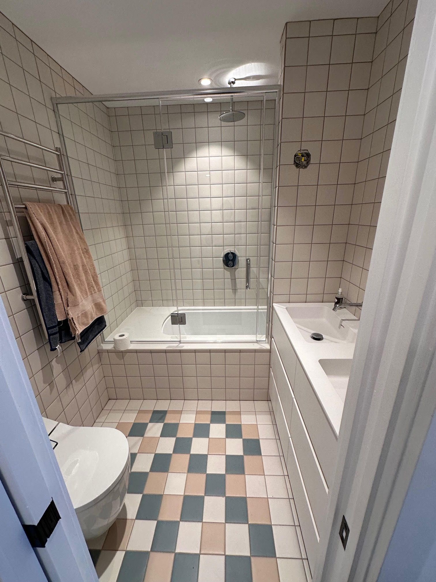 Small bathroom with tiled walls, bathtub, shower, toilet, and vanity. Floor has checkered pattern.