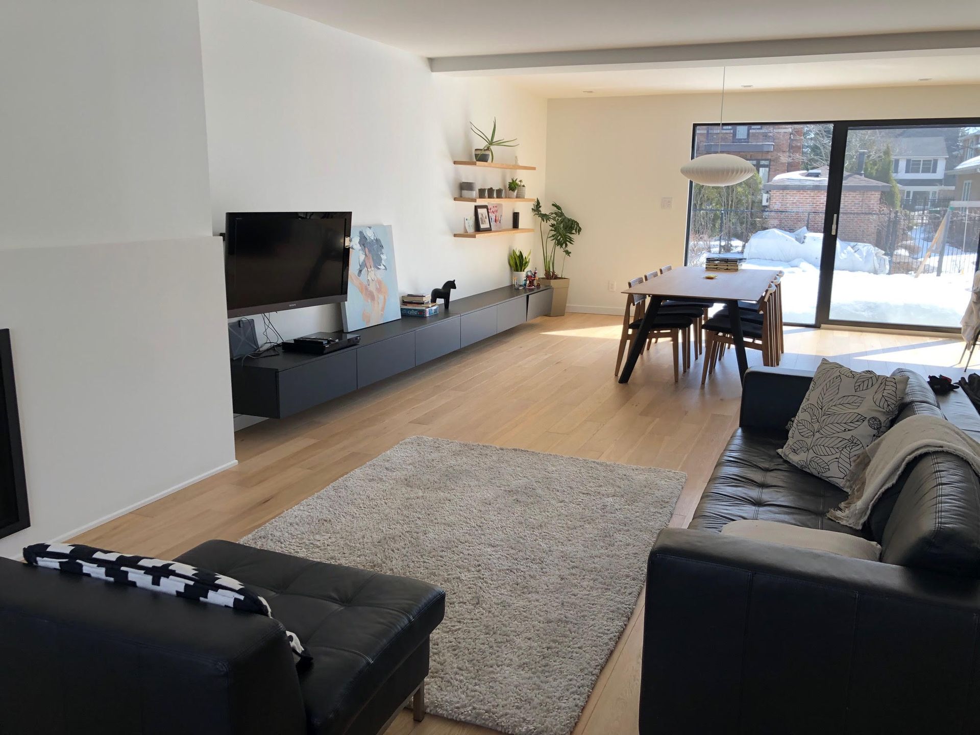 Modern living room with black furniture, wooden floor, and a snow-covered exterior visible through sliding glass doors.