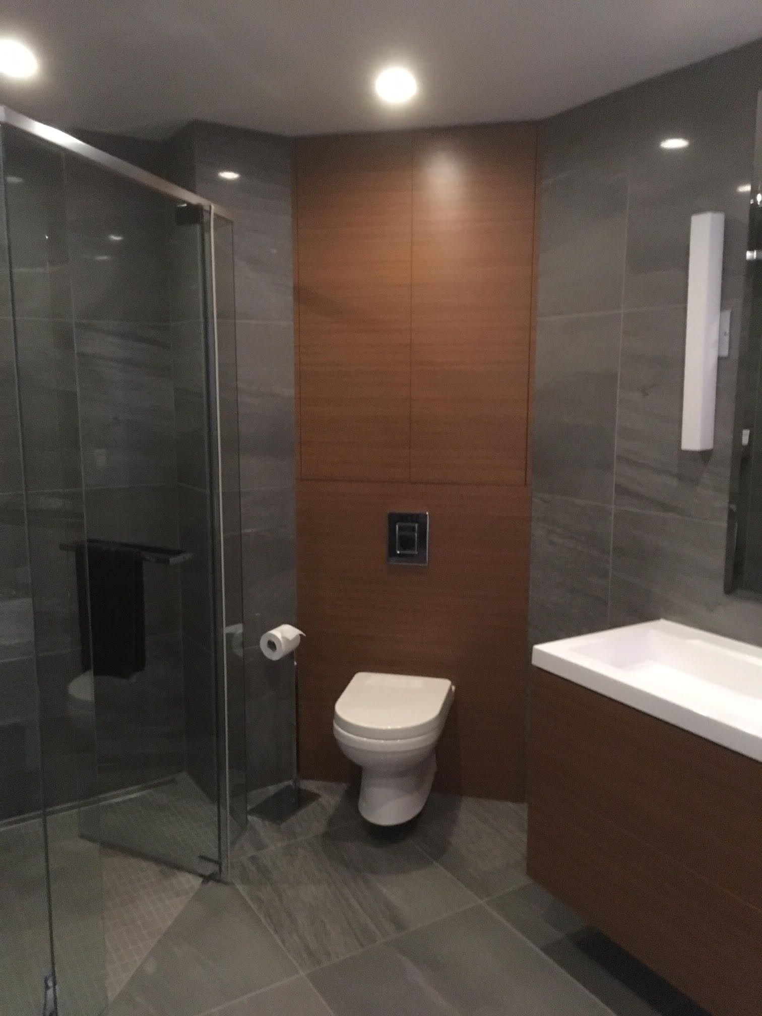 Modern bathroom with gray tile, shower, toilet, and vanity. Brown wall with toilet flush.
