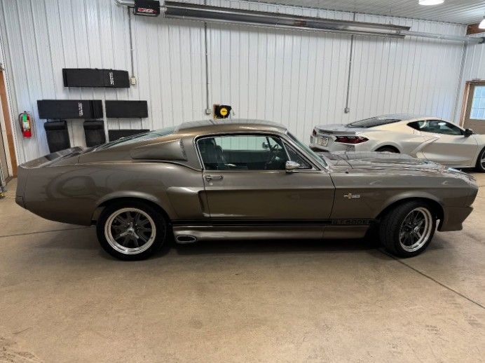 Classic gray muscle car parked inside a garage next to a white sports car.