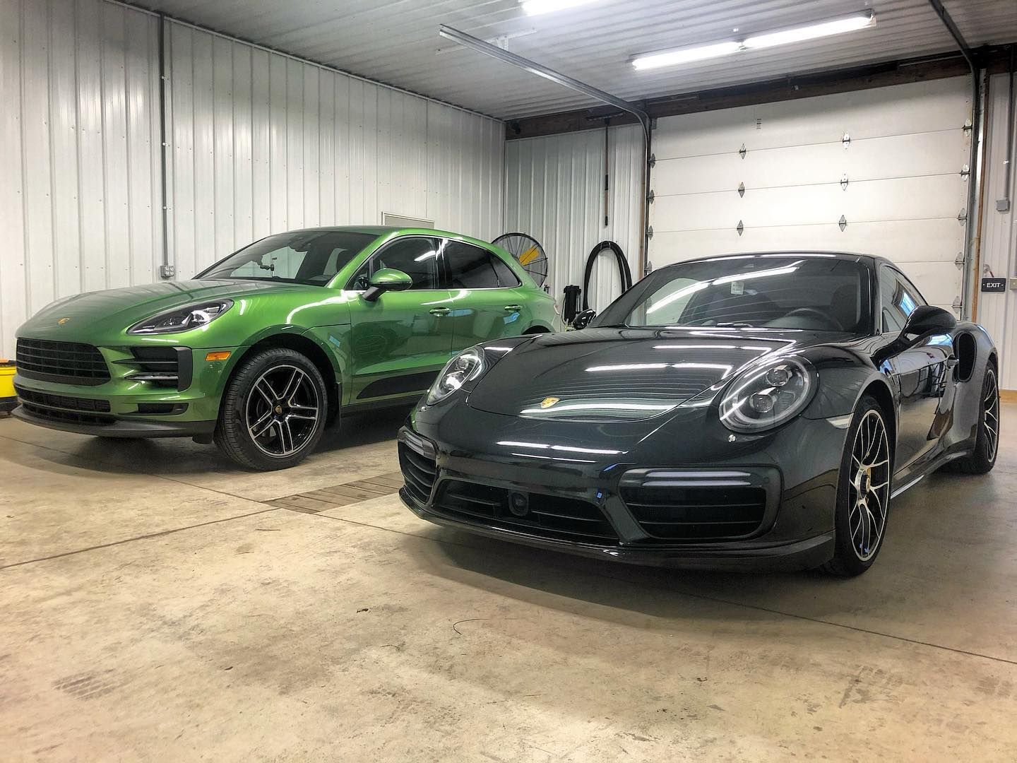 Two Porsche cars, a green SUV and a dark gray sports car, inside a garage.