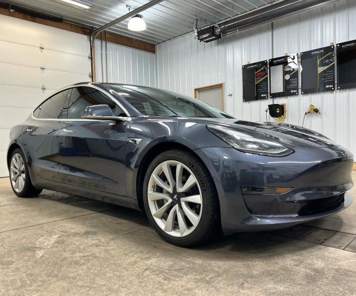 Dark blue Tesla sedan parked inside a garage with corrugated metal walls