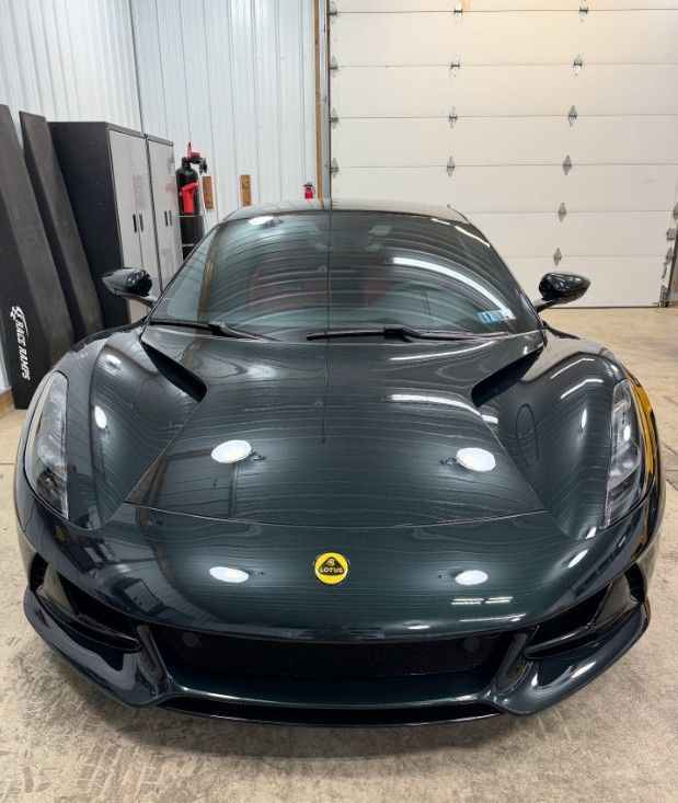 Front view of a dark gray Lotus sports car parked indoors in a garage.