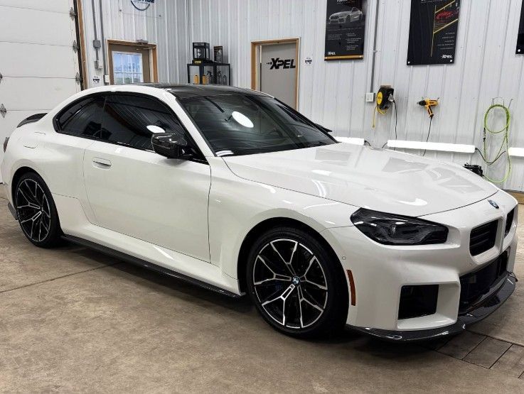 White sports sedan in a garage, front three-quarter view, with black wheels and a sleek body kit