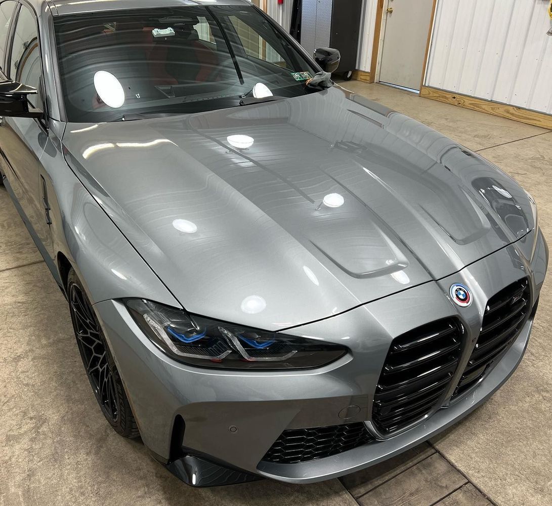 Gray BMW M3 sedan, front view, shiny body, black grill, indoor setting.