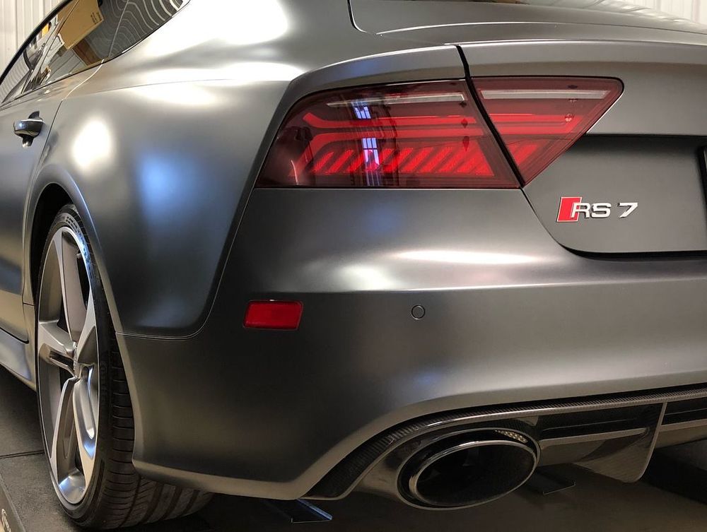 Close-up of a matte gray Audi RS7 sports car rear. Visible taillights, exhaust, and wheel.