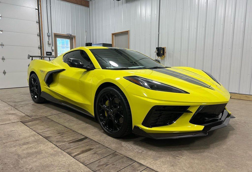 Yellow Corvette sports car with black racing stripe, parked inside a garage.