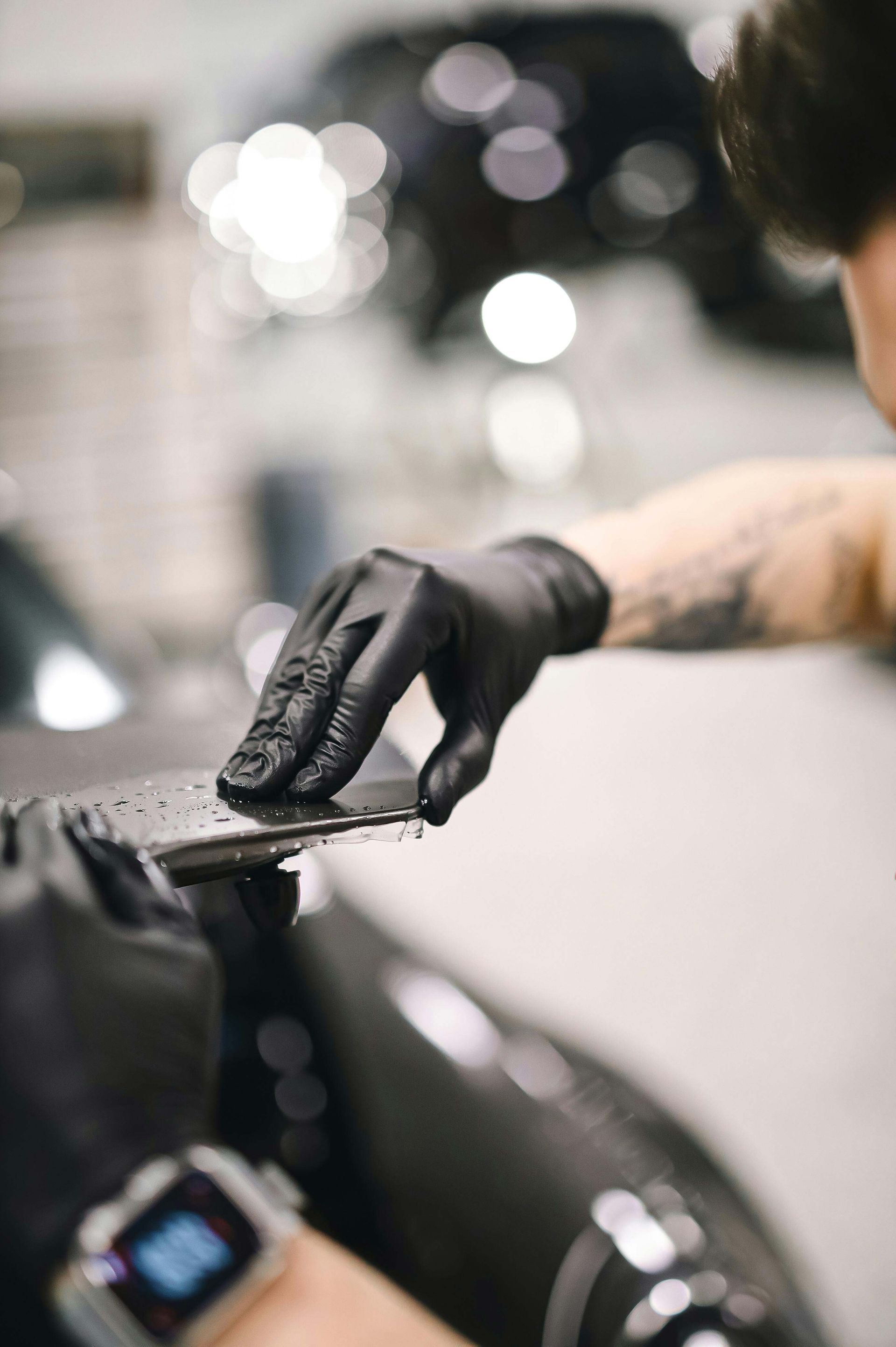 Gloved hand wiping a black car with a cloth in a garage setting