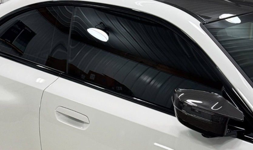 White car with tinted windows, carbon fiber mirror, and black roof.