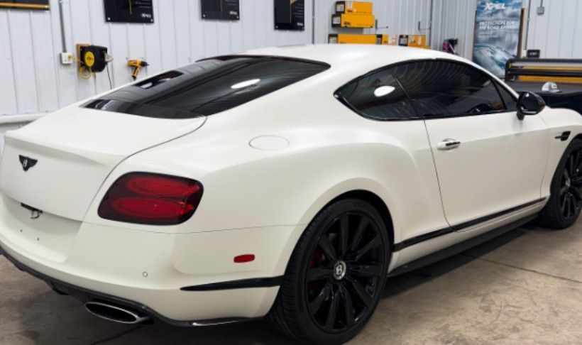 White Bentley coupe with black rims and tinted windows in a garage.