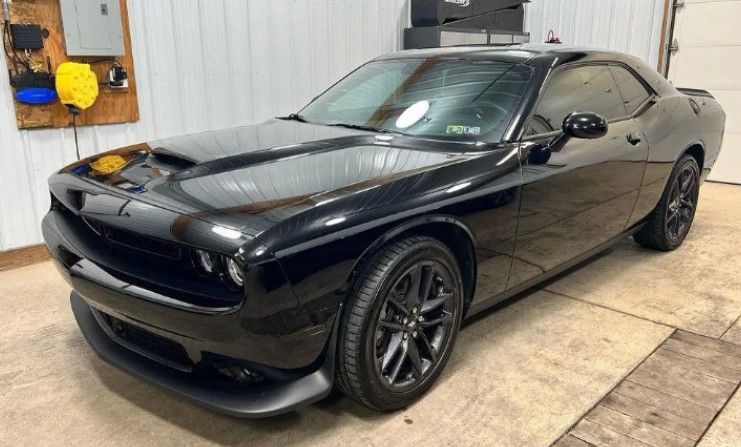Black Dodge Challenger parked indoors on a concrete floor, front-left view