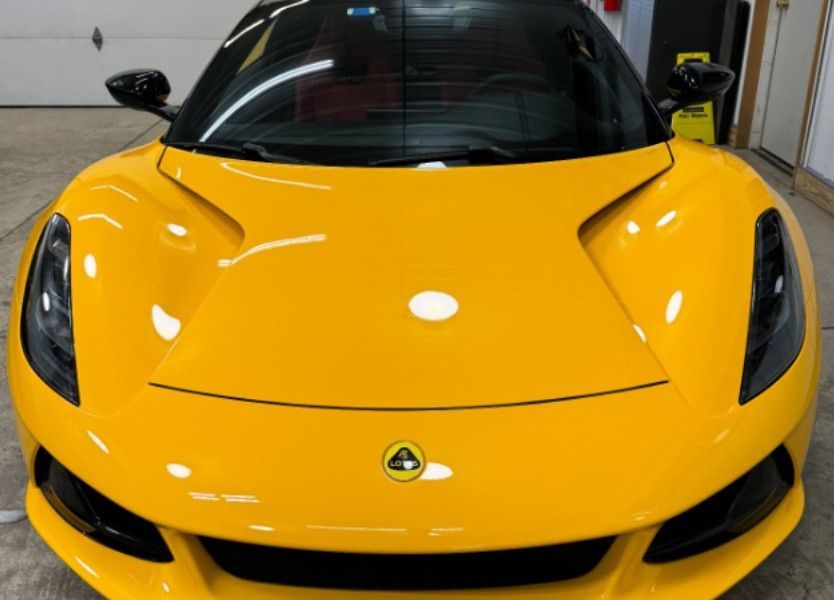 Yellow Lotus sports car, front view, shiny paint. Black windshield, black side mirrors, indoors.