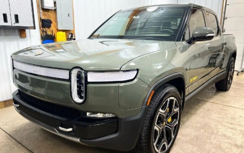 Green Rivian R1T electric pickup truck in a garage.