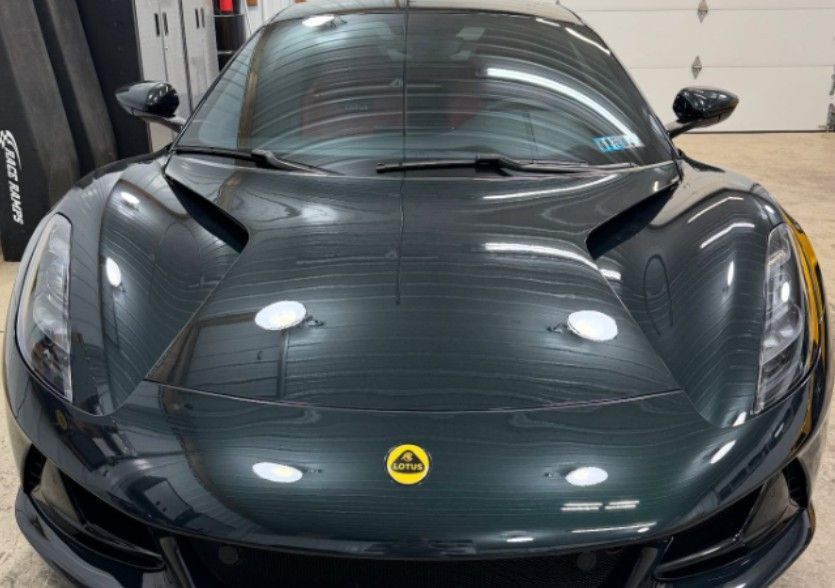 Dark green Lotus sports car, front view, with yellow emblem, in a garage.