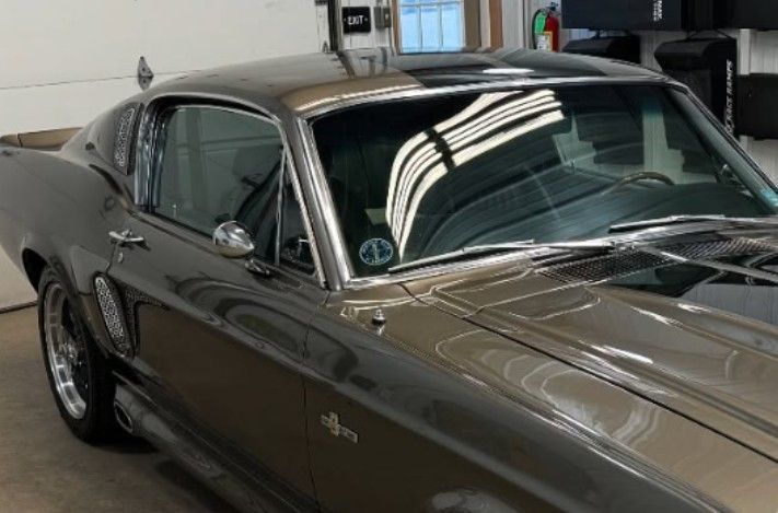 Dark gray 1967 Ford Mustang Shelby GT500 in a garage, shiny paint, chrome accents.