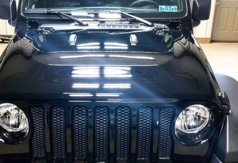 Black Jeep Wrangler hood, grille, and headlights reflecting overhead lights.