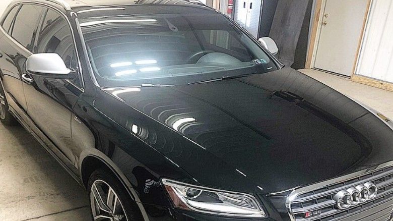 Dark gray Audi SQ5 SUV parked indoors, shiny black paint, tinted windows, silver side mirrors.