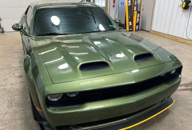 Green Dodge Challenger in a garage, front view with hood scoops and black racing stripe accents