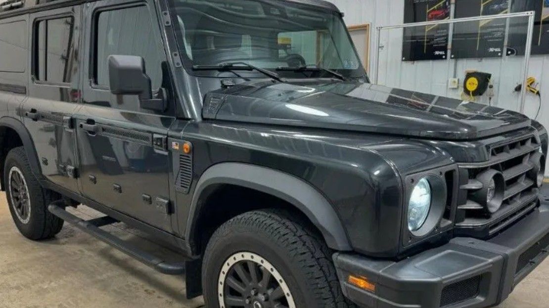 Dark gray Ineos Grenadier SUV, parked indoors, angled shot.