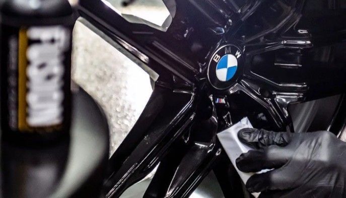 Black BMW wheel being cleaned with a brush and cloth by a gloved hand
