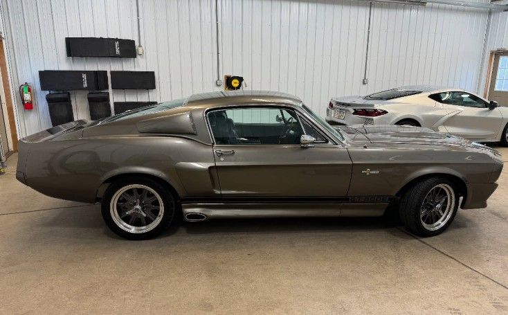 Brown 1960s Shelby Mustang in a garage, next to a white sports car.