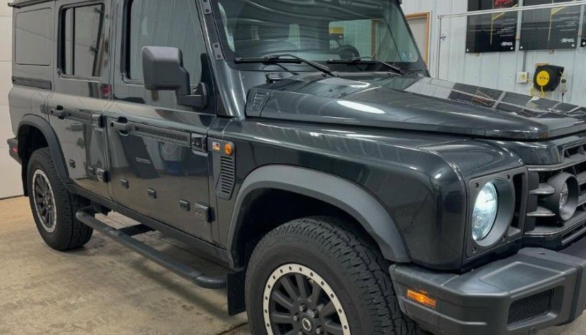 Dark gray Ineos Grenadier SUV, parked indoors, angled view.