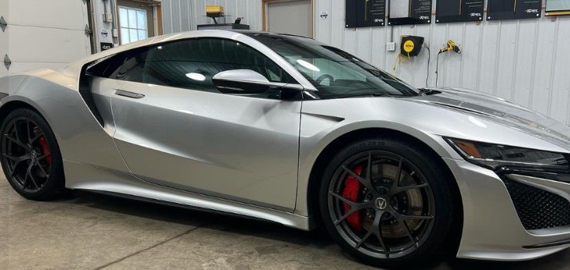 Silver Acura NSX sports car parked inside a garage, showing side view, red brake calipers.