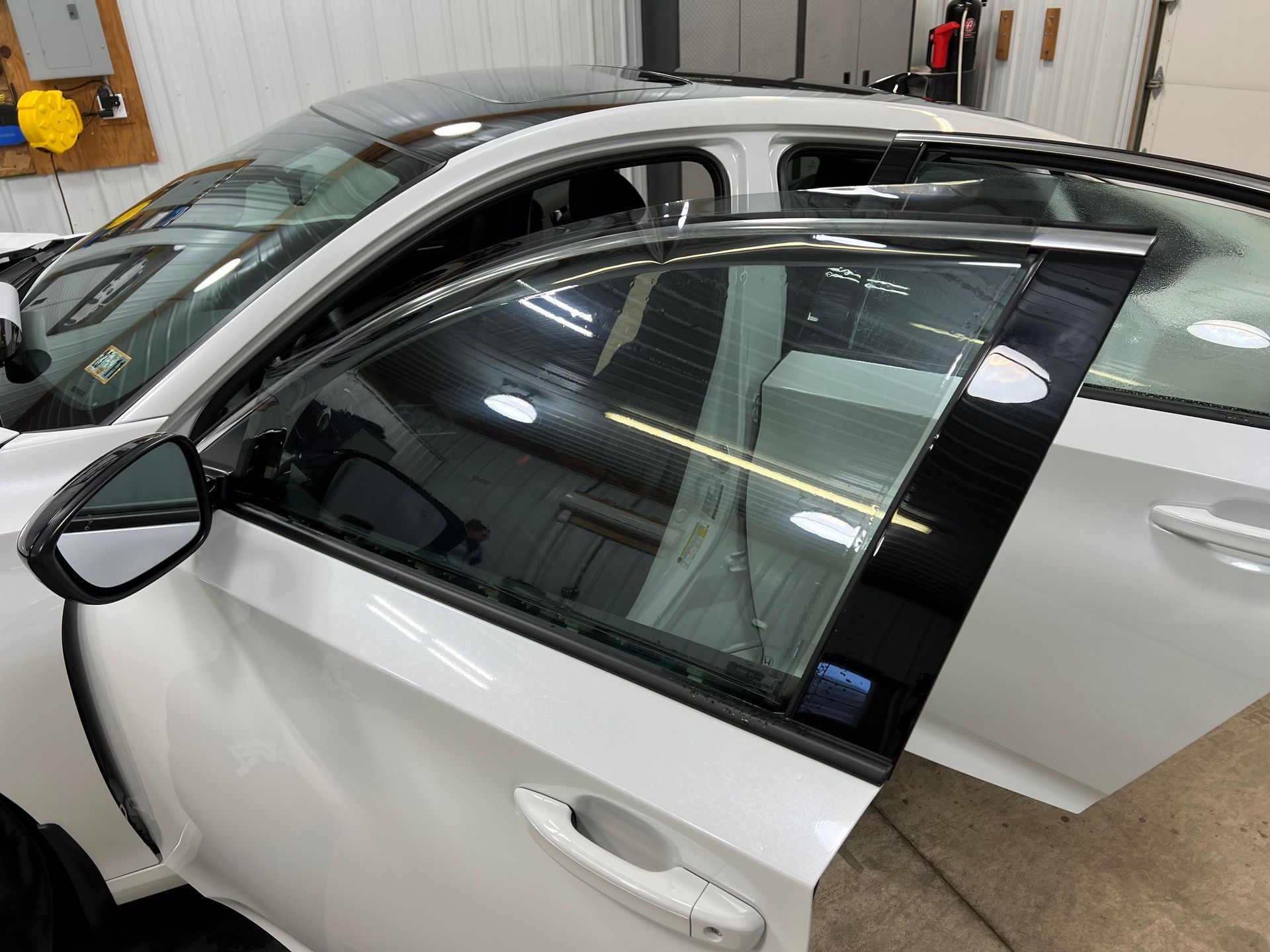 White sedan in a garage with the driver’s door open, showing the interior and side mirror.